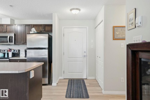 Open-concept living area featuring wood-finish flooring and a kitchen with dark cabinetry, stainless steel appliances, and a peninsula with a light-toned countertop - 1223 9363 Simpson Dr, Edmonton, AB 