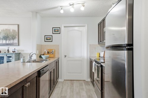 Kitchen with wood-finish flooring, dark wood cabinetry, stainless steel appliances, and track lighting - 1223 9363 Simpson Dr, Edmonton, AB 
