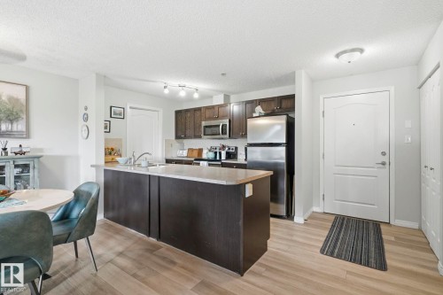 Open-concept kitchen and dining area featuring wood-finish flooring, dark wood cabinetry, a center island with sink, and stainless steel appliances - 1223 9363 Simpson Dr, Edmonton, AB 