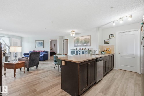 Kitchen island with dark wood-finish cabinetry, integrated stainless steel dishwasher, and a light-toned countertop - 1223 9363 Simpson Dr, Edmonton, AB 