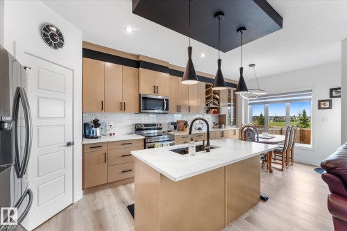 Contemporary kitchen featuring a central island with a sink, light wood-finish cabinetry, stainless steel appliances, and a white subway tile backsplash - 92 Elm Street, Fort Saskatchewan, AB 