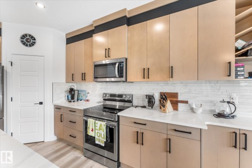 Modern kitchen featuring light wood-finish cabinetry with black hardware, white countertops, and a full suite of stainless steel appliances - 92 Elm Street, Fort Saskatchewan, AB 