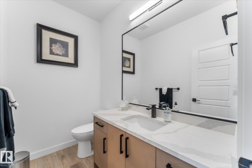 Modern vanity featuring a white countertop with integrated sink, black matte faucet, and wood-finish cabinetry with black hardware - 92 Elm Street, Fort Saskatchewan, AB 