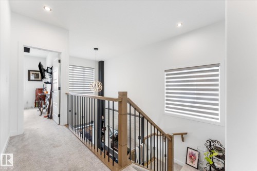 Upper-level hallway featuring a light wood newel post and handrail with black metal balusters - 92 Elm Street, Fort Saskatchewan, AB 