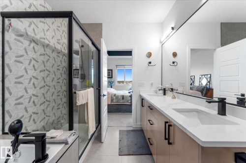 Spacious bathroom featuring a double vanity with matte black fixtures, an expansive mirror, and a large shower with patterned tile and a black-framed glass enclosure - 92 Elm Street, Fort Saskatchewan, AB 