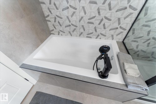 Built-in white bathtub featuring matte black fixtures, a handheld shower, and a textured tile surround - 92 Elm Street, Fort Saskatchewan, AB 