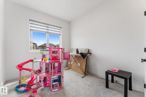 Bright interior room featuring a large window with horizontal blinds, light gray wall-to-wall carpeting, white painted walls, and a black paneled door with matte black hardware - 92 Elm Street, Fort Saskatchewan, AB 