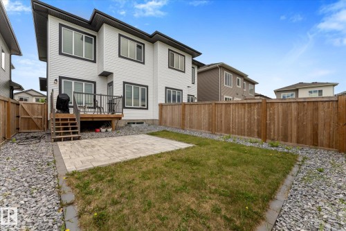 Rear exterior featuring white siding with dark trim, a wooden deck with dark railings, and a ground-level paver patio - 92 Elm Street, Fort Saskatchewan, AB 