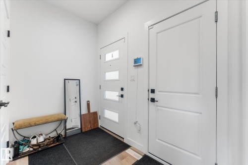 Entryway featuring a modern front door with frosted glass inserts, a classic panel door with matte black hardware, light wood-finish flooring, and crisp white walls - 92 Elm Street, Fort Saskatchewan, AB 