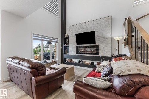 Vaulted ceilings with an upper transom window, stone-accented fireplace with built-in shelving, wood-finish flooring, and a staircase with wood handrails and wrought iron spindles - 92 Elm Street, Fort Saskatchewan, AB 