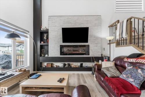 Living area featuring a floor-to-ceiling fireplace with an electric insert, a mounted television, and a white stacked stone surround - 92 Elm Street, Fort Saskatchewan, AB 