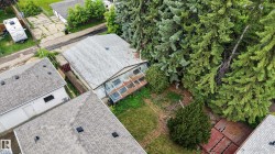 The property features a shingle roof, a greenhouse structure, a backyard with grass and mature trees, and a wooden fence boundary - 
