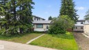 Single-story residence featuring a neutral exterior, a dark shingle roof, and multiple mature evergreen trees - 10924 154 Street, Edmonton, AB 