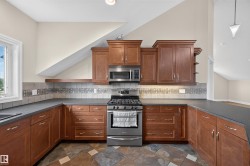 Kitchen featuring rich wood cabinetry, stainless steel appliances, dark countertops, and a patterned tile backsplash - 