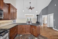Kitchen featuring wood cabinetry, dark countertops, tiled backsplash, stainless steel gas range, and slate-style flooring - 
