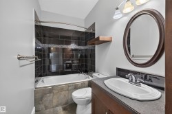 Bathroom featuring a dark subway tile shower surround with an accent mosaic stripe, a built-in tub, and a floating wood shelf - 