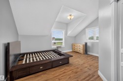 Attic space featuring wood-finish flooring, two windows with blinds, and white walls with sloped ceilings - 