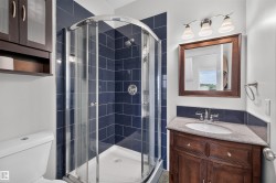 Bathroom featuring a curved glass shower enclosure, blue subway tile, a wood-finish vanity with a stone countertop, a framed mirror, and a three-light vanity fixture - 