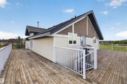 Spacious outdoor deck featuring natural wood planks, a white railing system, and a siding exterior with shake accents - 