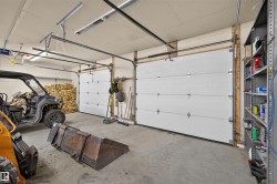 Spacious garage featuring two overhead doors with automatic openers, exposed wood beam construction, concrete flooring, and built-in metal shelving - 
