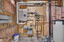 Utility room featuring a modern tankless water heater, intricate copper piping, electrical panel, and a water heater tank - 