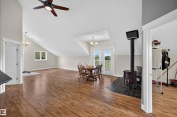 Spacious open-concept room featuring wood-finish flooring, a vaulted ceiling, and a cast-iron stove with a black tile hearth - 