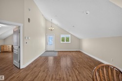Vaulted ceilings enhancing the spacious interior, featuring wood-finish flooring, recessed lighting, and a prominent entry door with decorative glass - 