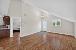 Vaulted ceilings enhance this open concept area featuring wood-finish flooring, light-toned walls, and a prominent window - 