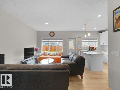 Open-concept living area featuring light wood-finish flooring, recessed lighting, and a white kitchen with pendant lights - 2039 13 Avenue, Edmonton, AB 