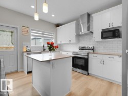 Kitchen featuring white cabinetry, wood-finish flooring, stainless steel appliances, a center island with a light wood-finish countertop, and a subway tile backsplash - 