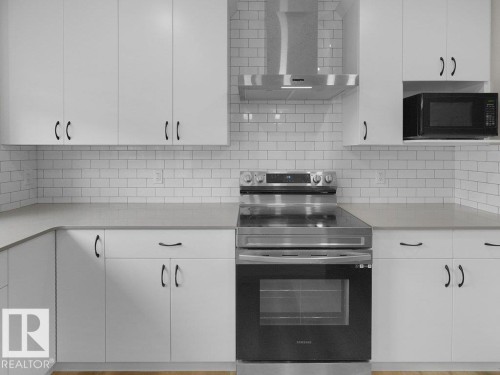 Modern kitchen featuring white shaker-style cabinetry, a subway tile backsplash, stainless steel appliances, light-toned countertops, and wood-finish flooring - 2039 13 Avenue, Edmonton, AB 