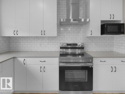 Modern kitchen featuring white shaker-style cabinetry, a subway tile backsplash, stainless steel appliances, light-toned countertops, and wood-finish flooring - 