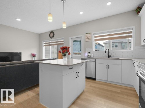 Open-concept kitchen and living area featuring a central island, light wood-finish flooring, white cabinetry with black hardware, and a subway tile backsplash - 2039 13 Avenue, Edmonton, AB 