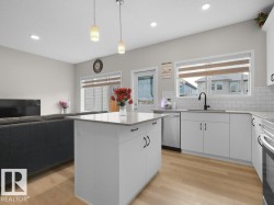 Open-concept kitchen and living area featuring a central island, light wood-finish flooring, white cabinetry with black hardware, and a subway tile backsplash - 