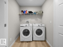 Dedicated laundry area featuring light wood-finish flooring, light gray walls, and a white wire shelving unit - 