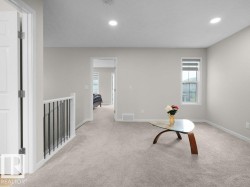 Spacious carpeted upper-level area featuring recessed lighting, a white baluster with black iron spindles, and a window with blinds - 