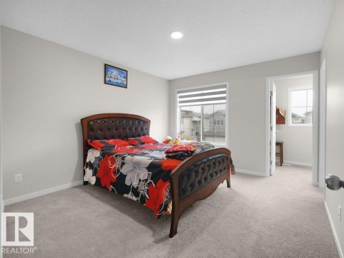 Carpeted bedroom featuring light gray walls, a window with horizontal blinds, an overhead recessed light, and a doorway to an additional room - 2039 13 Avenue, Edmonton, AB 
