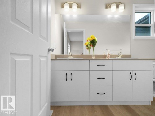 Bathroom vanity featuring dual under-mount sinks with chrome faucets, a large wall-mounted mirror, and overhead sconce lighting - 2039 13 Avenue, Edmonton, AB 