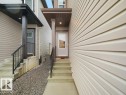 Light-toned siding exterior featuring a covered entry with a white paneled door, concrete steps, and a black metal handrail - 2039 13 Avenue, Edmonton, AB 