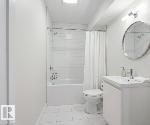 Bathroom featuring white subway tile surround, white ceramic tile flooring, a white vanity with integrated sink, and a circular wall-mounted mirror - 2039 13 Avenue, Edmonton, AB 