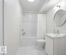 Bathroom featuring white subway tile surround, white ceramic tile flooring, a white vanity with integrated sink, and a circular wall-mounted mirror - 