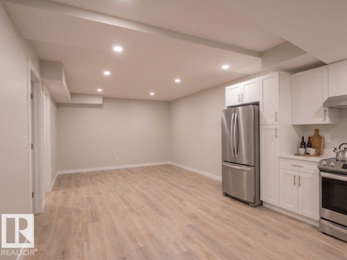 Open-concept living space featuring wood-finish flooring, recessed lighting, and a kitchen area with white cabinetry and stainless steel appliances - 2039 13 Avenue, Edmonton, AB 