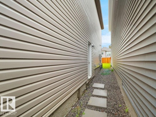 Side yard access featuring a gravel pathway with stepping stones, light-toned horizontal siding, and a rear entry door - 2039 13 Avenue, Edmonton, AB 