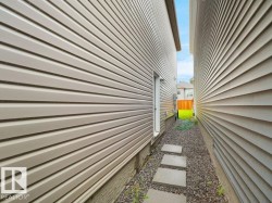 Side yard access featuring a gravel pathway with stepping stones, light-toned horizontal siding, and a rear entry door - 