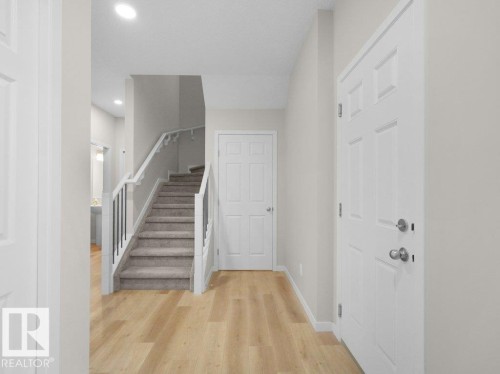 Entryway featuring wood-finish flooring, a carpeted staircase with white risers and black balusters, and a paneled entry door - 2039 13 Avenue, Edmonton, AB 