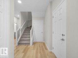 Entryway featuring wood-finish flooring, a carpeted staircase with white risers and black balusters, and a paneled entry door - 