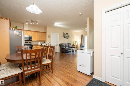 Open-concept living area featuring wood-finish flooring, a kitchen with light wood cabinetry and stainless steel appliances, and a double-door closet - #117 226 Macewan Sw, Edmonton, AB - Indoor Photo Showing Other Room