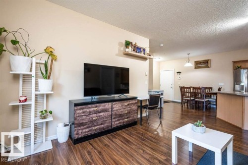 Open-concept living space featuring wood-finish flooring, a dining area with a chandelier-style pendant light, and a kitchen island with an integrated breakfast bar - #117 226 Macewan Sw, Edmonton, AB - Indoor Photo Showing Living Room
