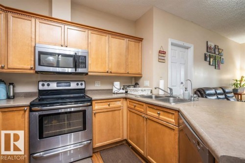 Kitchen featuring wood cabinetry, stainless steel appliances, a double basin sink, and laminate countertops - #117 226 Macewan Sw, Edmonton, AB - Indoor Photo Showing Kitchen With Double Sink