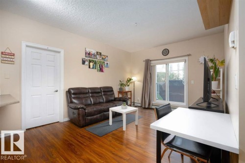 Living area featuring wood-finish flooring, a white six-panel interior door, and a sliding glass door with vertical blinds - #117 226 Macewan Sw, Edmonton, AB - Indoor Photo Showing Living Room